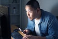 Young Asian man using smart phone and computer until late night, he is working or studying hard to reach his ambition. Student or Royalty Free Stock Photo