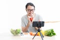 Young Asian man vlogger and recording video during cooking healthy vegan meal for food channel. Influencer marketing concept