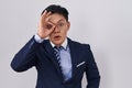 Young asian man wearing business suit and tie doing ok gesture shocked with surprised face, eye looking through fingers Royalty Free Stock Photo