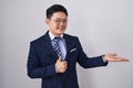 Young asian man wearing business suit and tie showing palm hand and doing ok gesture with thumbs up, smiling happy and cheerful Royalty Free Stock Photo