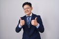 Young asian man wearing business suit and tie success sign doing positive gesture with hand, thumbs up smiling and happy Royalty Free Stock Photo