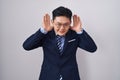 Young asian man wearing business suit and tie trying to hear both hands on ear gesture, curious for gossip