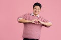 Young asian man wearing casual pink sweater smiling in love doing heart symbol shape with hands. romantic concept Royalty Free Stock Photo