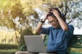 Young asian man working with his laptop and angry about online business profits  on a bench in the park outdoors on vacation time Royalty Free Stock Photo