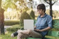 Young asian man working with his laptop on a bench in the park outdoors on vacation time Royalty Free Stock Photo