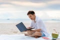 Young asian man working outdoor during his vacation time by laptop while sitting on the beautiful beach. Summer, holidays, Royalty Free Stock Photo