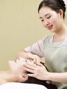 Young asian masseur performing face massage on woman