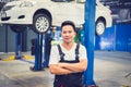 Young Asian mechanic who standing in the auto service company with car lifting on a hoist background