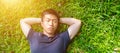 Young asian men lies on green moss relaxing with eyes closed and hands behind his head, feeling comfortable on the grass field Royalty Free Stock Photo