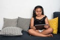 Young asian/mixed girl sitting on sofa using tablet with head phones Royalty Free Stock Photo