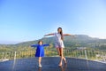 Young Asian mom and daughter feeling free with arms wide open at beautiful trees and mountains on blue sky