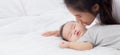 Young asian mother kiss cheek of little baby girl with tender on bed in the bedroom, mom love newborn and care. Royalty Free Stock Photo