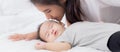 Young asian mother kiss cheek of little baby girl with tender on bed in the bedroom, mom love newborn and care. Royalty Free Stock Photo