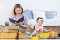 Young Asian mother is packing her merchandise product package while working at home ready to deliver while her toddler kid is Royalty Free Stock Photo