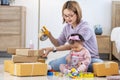 Young Asian mother is packing the merchandise product package while working at home ready to deliver while her toddler kid is Royalty Free Stock Photo