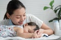 Young Asian mother smiling and looking at her cute Caucasian little baby girl sleeping and holding mother`s finger in hand Royalty Free Stock Photo