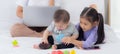 Young asian mother working at home online to internet with laptop computer and talking phone and daughter looking tablet. Royalty Free Stock Photo