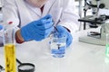 Young Asian muslim female scientist holding blue reagent dropper with beaker