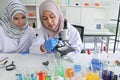 Young Asian muslim female scientist holding blue reagent dropper working on microscope