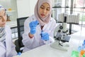 Young Asian muslim female scientist holding blue reagent dropper working on microscope