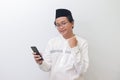 young Asian muslim man raising his fist, celebrating winning game or getting good news on his mobile phone. Isolated Royalty Free Stock Photo