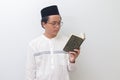 young Asian muslim man reading and reciting Holy book of Quran seriously. Isolated image on white background