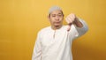 Young asian muslim man shows upset expression with thumbs down, against yellow background