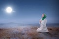 Young asian muslim woman sitting in pray position while raised hands and praying on the sand dune Royalty Free Stock Photo