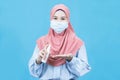 Young asian muslim woman in traditional dress wearing medical face mask holding Alcohol Spray Bottle isolated on blue background Royalty Free Stock Photo