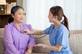 Young asian nurse or caregiver sitting on sofa holding stethoscope listen heartbeat with senior woman in living room. Royalty Free Stock Photo