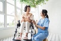 Young Asian nurse talking to a smiling senior female patient on a wheelchair and comforting her. Royalty Free Stock Photo