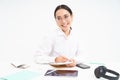 Young asian office woman, sitting at workplace desk, making notes, smiling and looking professional, white background Royalty Free Stock Photo