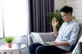 Young Asian people work on laptops with video calling for meetings, and sitting on the sofa at home