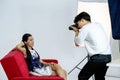 Young asian photographer is photographing a model posing on a red sofa for advertising in a magazine Royalty Free Stock Photo