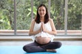 Young asian pregnant woman sitting and close her eyes in living room and enjoying in meditates indoor with yoga pose or stretching Royalty Free Stock Photo