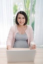 Young Asian pregnant woman working from home using computer and drinking milk for good health of her baby Royalty Free Stock Photo
