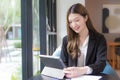 Young Asian professional  working female in a black suit is working on an tablet on the table smiling happily in the office and Royalty Free Stock Photo
