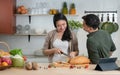 Young Asian romantic couple is cooking in the kitchen. Happy beautiful woman making healthy food like bread, fruits and salad Royalty Free Stock Photo