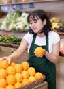 Young asian salesgirl arranging oranges on display in supermarket Royalty Free Stock Photo
