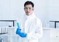 Young Asian scientist holds a scientific liquid in a glass tube. Complete protective equipment protective clothing, goggles,