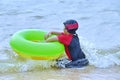 Young Asian sits in the surf on an ocean beach with her donut.