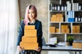 Young Asian SMEs woman holding parcels and looking to camera, standing among several boxes in modern office Royalty Free Stock Photo