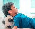 Young Soccer player kid is sleeping on a football under his head