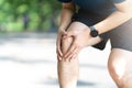 Young asian sporty man holding knee pain in running public nature park in the morning. Joint or leg injury in athlete or jogger