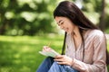 Young asian student girl sitting on lawn in park and writing notes Royalty Free Stock Photo