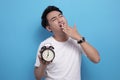 Young Asian man tired and yawning while holding alarm clock Royalty Free Stock Photo