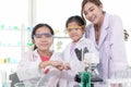 Happy young Asian student schoolgirls in lab coat with female scientist teacher bumping their fists together to celebrate success