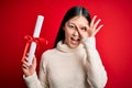 Young asian student woman holding graduate diploma over red  background with happy face smiling doing ok sign with hand on Royalty Free Stock Photo