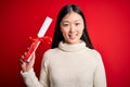 Young asian student woman holding graduate diploma over red isolated background with a happy face standing and smiling with a Royalty Free Stock Photo