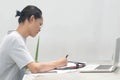 A focus young asian student and worker, doing homework with laptop notebook smartphone and paper at indoors with green plant Royalty Free Stock Photo